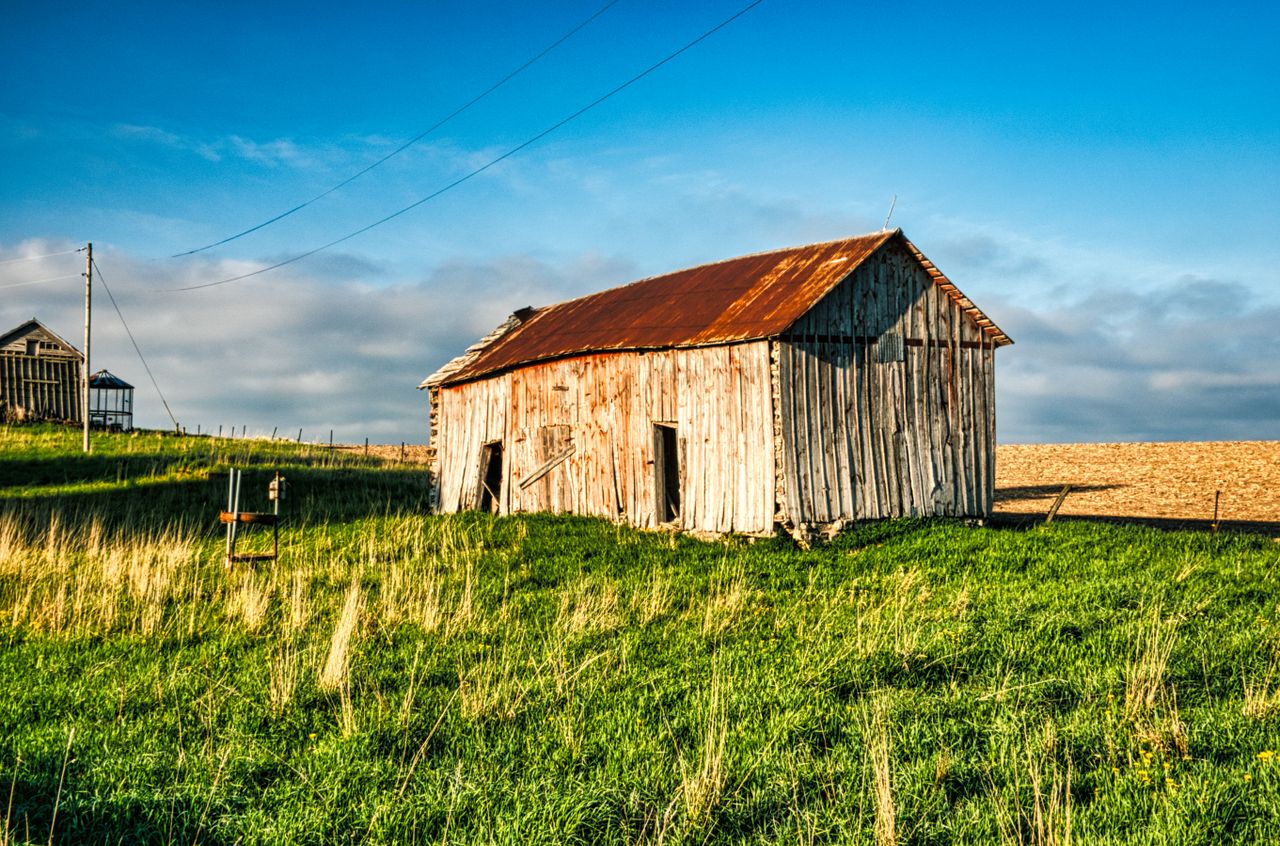 A picturesque rustic barn sits in a vibrant green field under a clear blue sky in rural Minnesota.